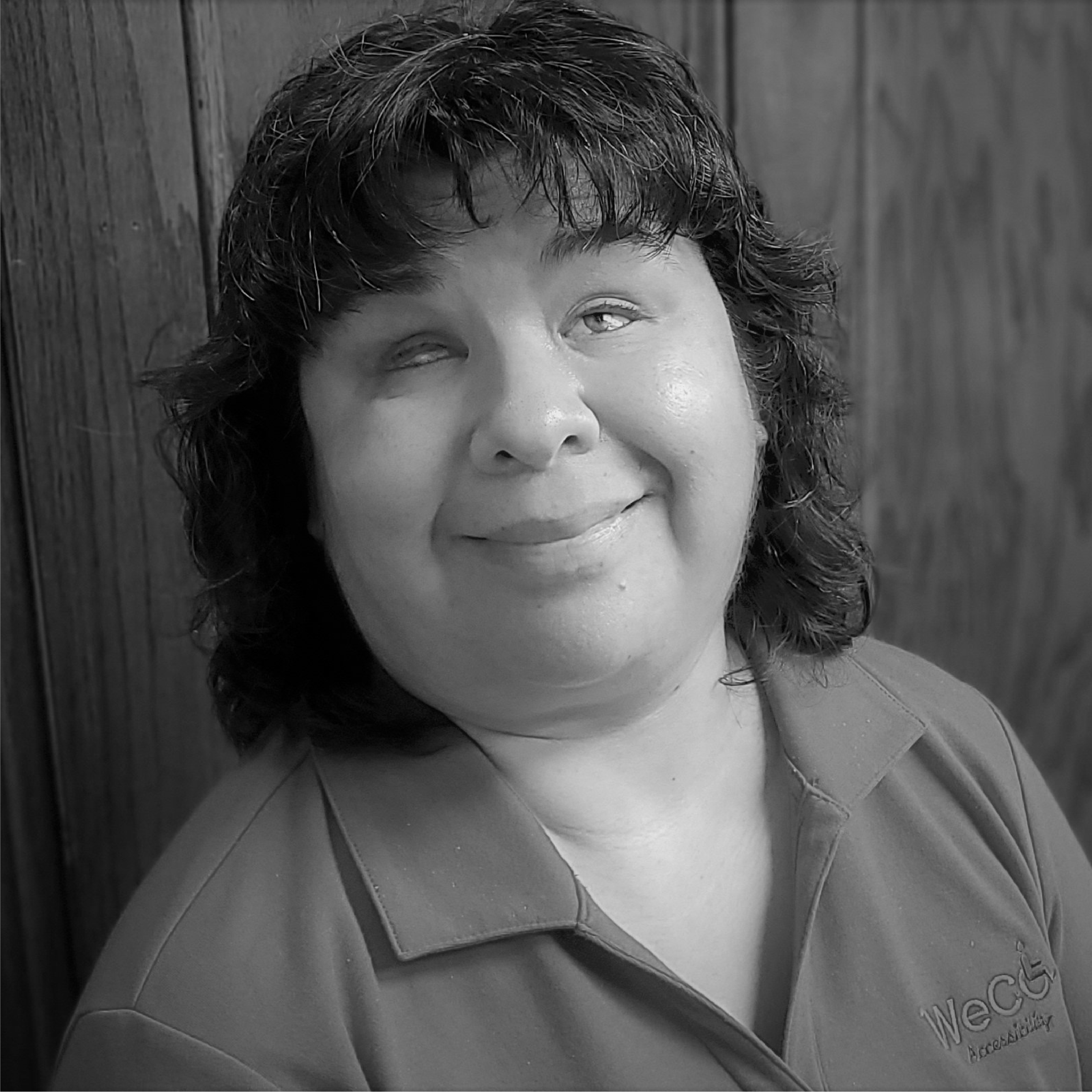 Black and white photo of Sue Ann Rodriquez wearing a collared polo and smiling widely. She has dark, shoulder length, wavy hair.